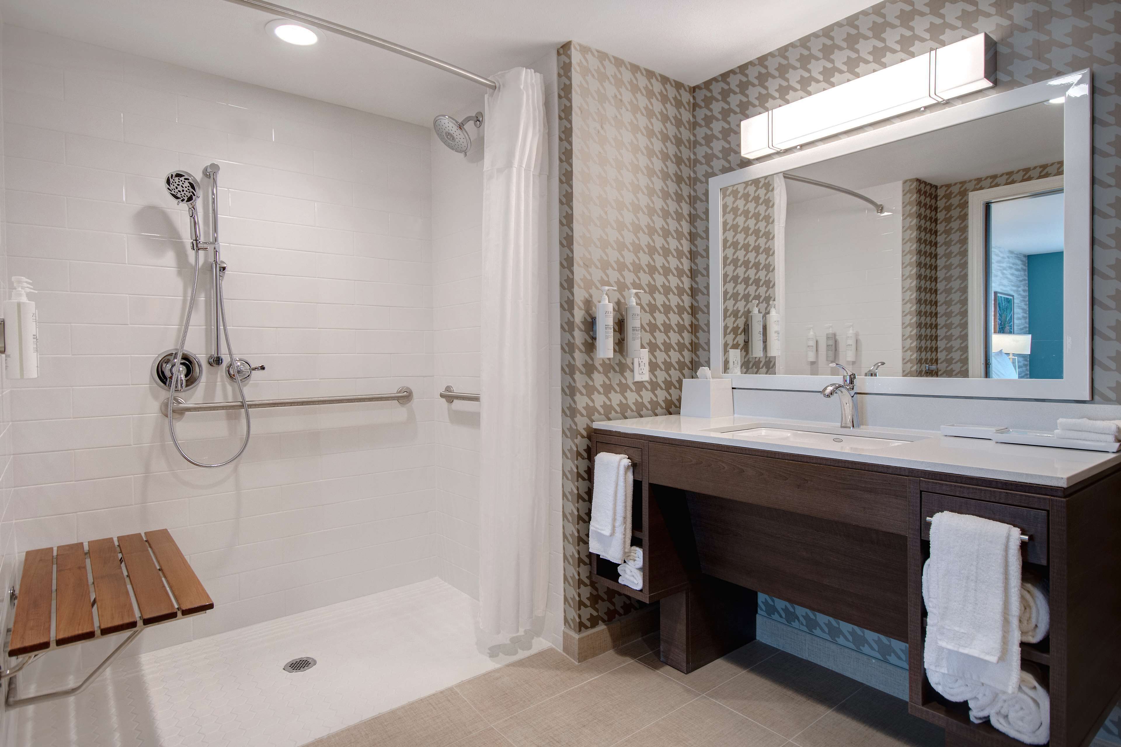 A modern bathroom with a walk-in shower, a large mirror, and a wooden bench.