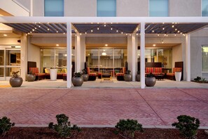 Entrada de hotel con zona de estar al aire libre techada, grandes macetas y un camino pavimentado con baldosas.