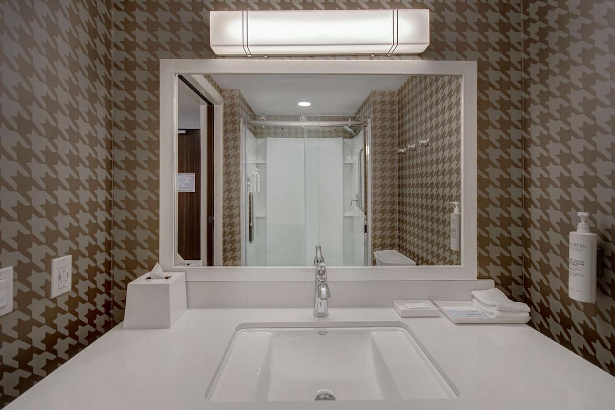Une salle de bain avec un grand miroir, un lavabo blanc et un papier peint à motifs.