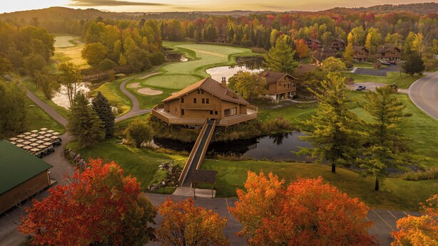 Un campo de golf con un club de campo, un estanque y follaje otoñal.