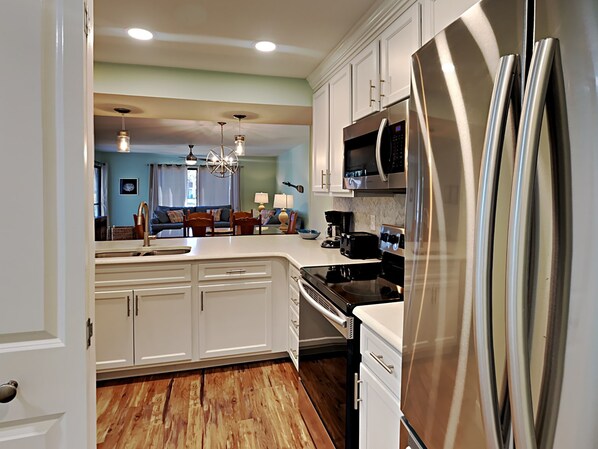 A modern kitchen with white cabinets, stainless steel appliances, and a wooden floor. - Edgewater Beach & Golf Resort IV by Resort Collection (Panama City Beach)