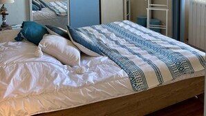 A bedroom with a bed, a mirror, a wall-mounted air conditioner, and a window with curtains.