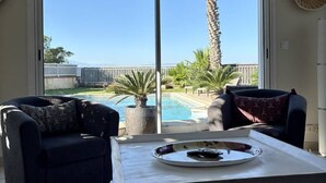 A living room with a view of a pool and palm trees, featuring two sofas, a coffee table, and a sliding glass door.