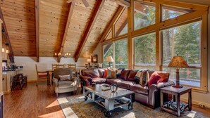 A spacious living room with a high ceiling, large windows, a leather sofa, and a coffee table. - Edelweiss - Remodeled Luxury 3 BR with Private Hot tub (Tahoe City)
