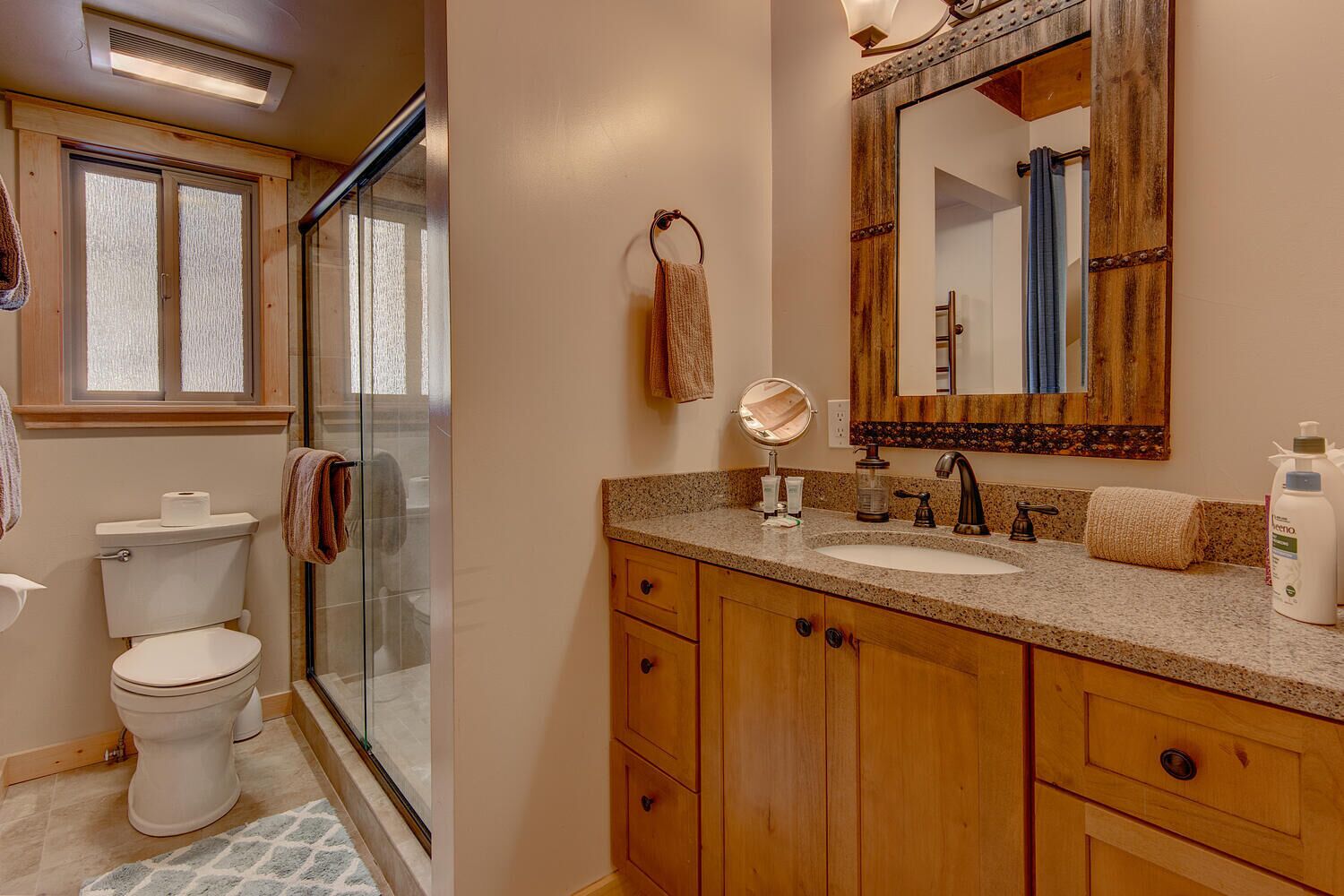 A bathroom with a glass shower enclosure, a toilet, a sink with a wooden vanity, and a large mirror.