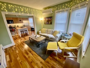 A cozy living room with a sofa, yellow armchair, and a coffee table. A kitchen with a dining area is visible in the background. - ⭐The Rhody Retreat⭐ Minutes from Downtown ⭐Modern, Spacious, Highly Rated!!!⭐ (Providence)