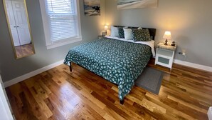 Une chambre à coucher avec un lit, des tables de chevet, une fenêtre avec des stores, une porte et des guirlandes lumineuses accrochées aux murs.