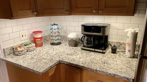 Une cuisine avec des meubles de rangement en bois, une machine à café, un pot de sucre, une boîte de céréales et un porte-essuie-tout.