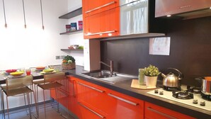 Een moderne keuken met oranje kastjes, roestvrijstalen apparatuur en een bar met krukken.
