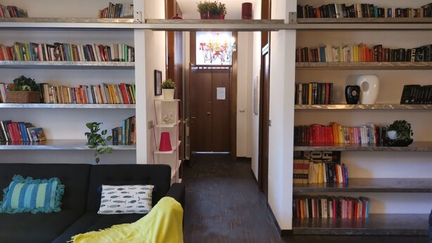 Een knus woongedeelte met een bank, een salontafel en een boekenplank vol boeken.