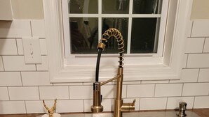 Una cucina con due lavelli in acciaio inossidabile, un rubinetto dorato e una finestra sopra il lavello.