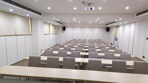 Un salón de conferencias con una larga mesa, sillas, un proyector y paredes blancas.