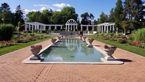 Um jardim formal com piscina central, pérgulas brancas e um gazebo.