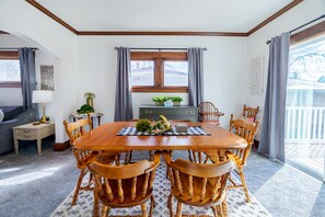 A dining room with a wooden table and chairs, a window with curtains, a small side table with a lamp, and a decorative plant on the windowsill. - King Bed, Stocked Kitchen, Easy Driveway Parking, 2mi to Downtown & Coliseum (Fort Wayne)