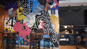 Interior de restaurante com mural, bancada de bar e área de cozinha.