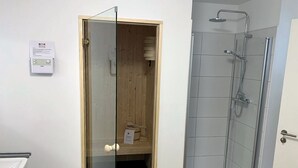 A bathroom with a glass shower enclosure, a wooden door, and a white sink. - 50.1.m Ankerplatz - Moderne, Hochwertige Ferienwohnung, Sauna, Großer Balkon, Strandnah (Wangerland)