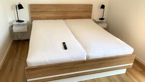 A single bed with a wooden headboard, white bedding, and two bedside tables with lamps. - 50.1.m Ankerplatz - Moderne, Hochwertige Ferienwohnung, Sauna, Großer Balkon, Strandnah (Wangerland)