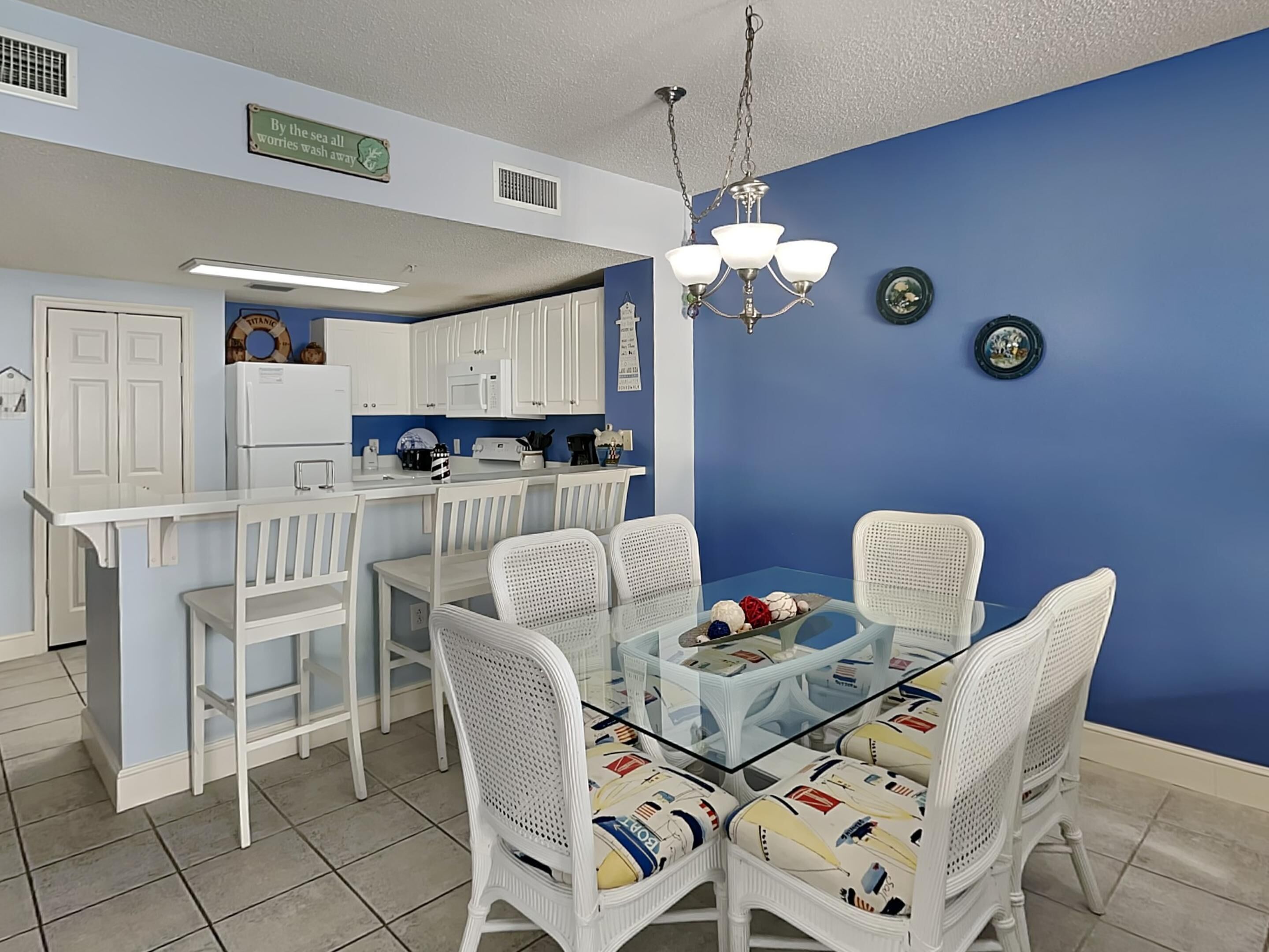A modern kitchen with white cabinets, a dining area with wicker chairs and a glass table, and a blue accent wall.