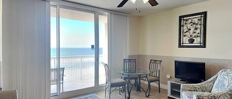 Una sala de estar con una mesa de centro de vidrio, un sofá, un televisor y un balcón con vista al océano.