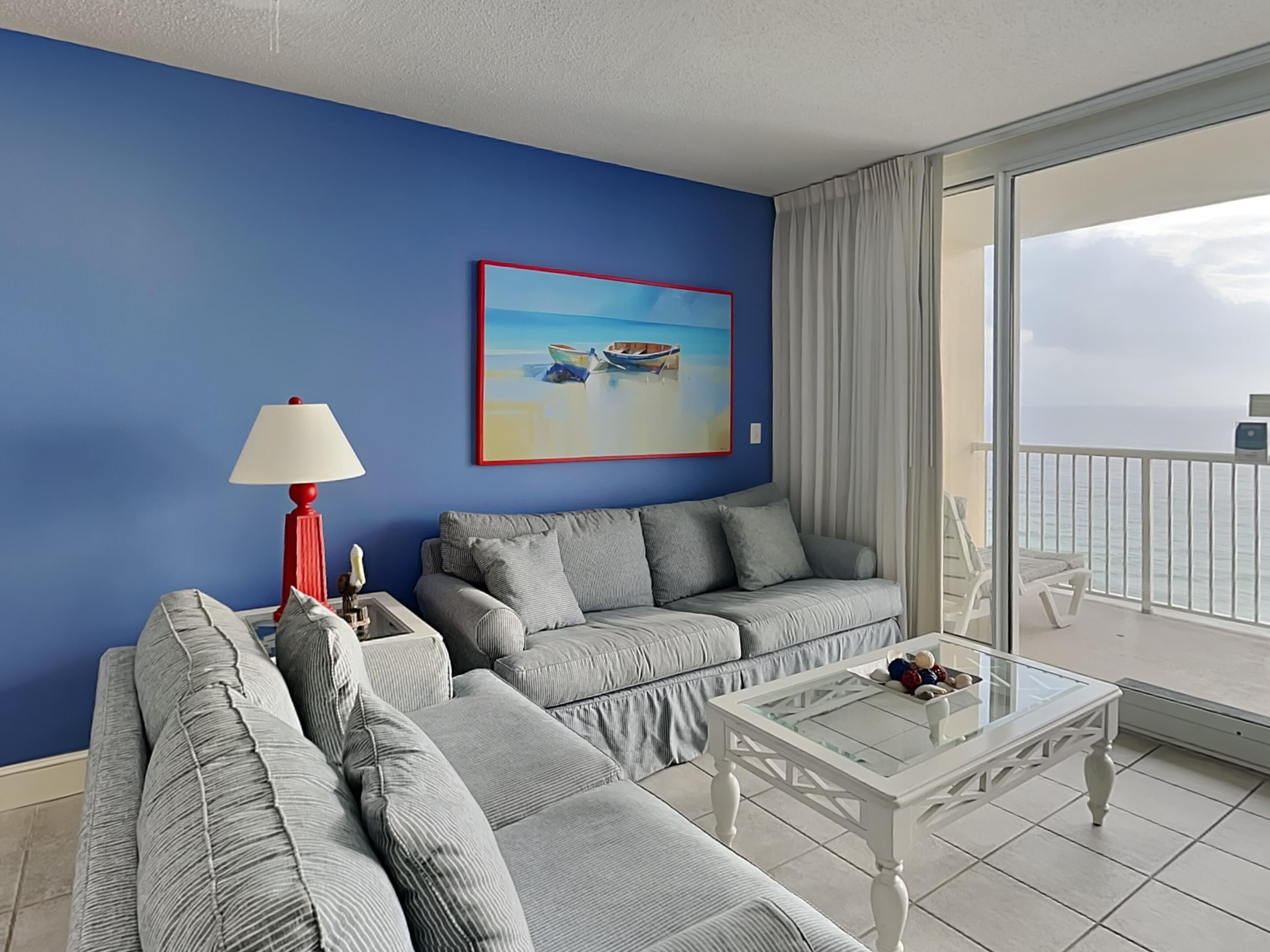 A modern living room with a blue wall, a grey sofa, a red lamp, and a glass coffee table.