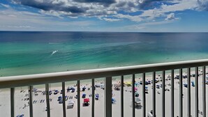 Vista da praia a partir de uma varanda, com águas turquesa cristalinas e uma praia arenosa com guarda-sóis e pessoas.