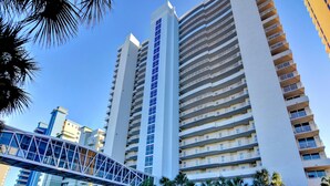 Um hotel moderno com vários andares, uma passarela para pedestres e palmeiras.