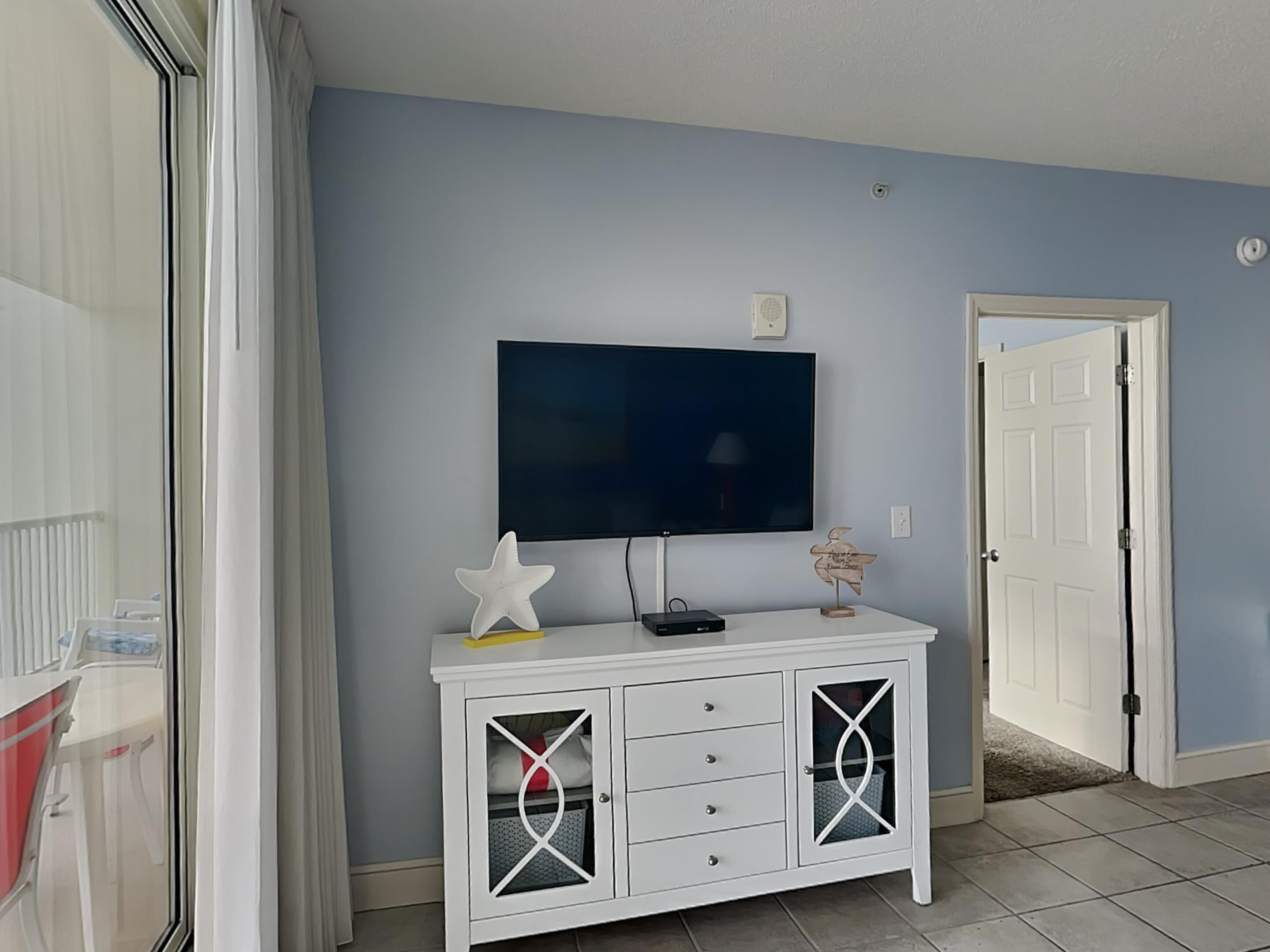A room with a white cabinet, a flat-screen TV mounted on the wall, and a door to the right.