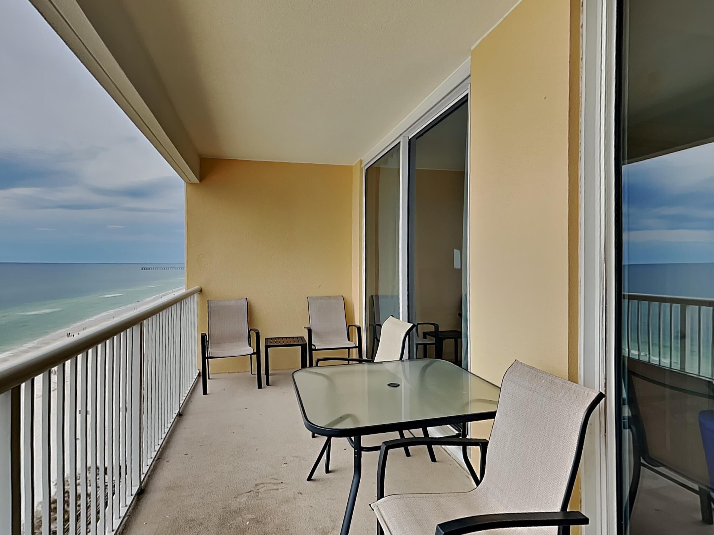 A balcony with a glass table and chairs, overlooking the ocean.