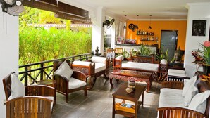 A cozy indoor seating area with wooden furniture, a fan, and a view of lush greenery outside. - Sekla Villa Angkor (Siem Reap)