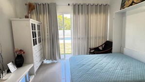 Une chambre à coucher avec un lit, une commode, une chaise et une fenêtre avec des rideaux.