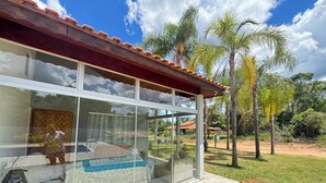 Une maison moderne dotée d’une grande baie vitrée, d’un toit en tuiles et d’une cour verdoyante agrémentée de palmiers.