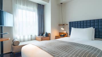 Une chambre d’hôtel avec un grand lit, une table de chevet, une lampe et un téléviseur posé sur un meuble.