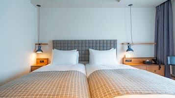 Un lit double avec une tête de lit capitonnée, deux tables de chevet avec des lampes, une horloge de chevet et un rideau sur le côté droit.