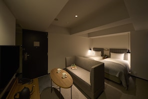 Een hotelkamer met een bed, een bank, een klein tafeltje met twee kopjes en een televisie.