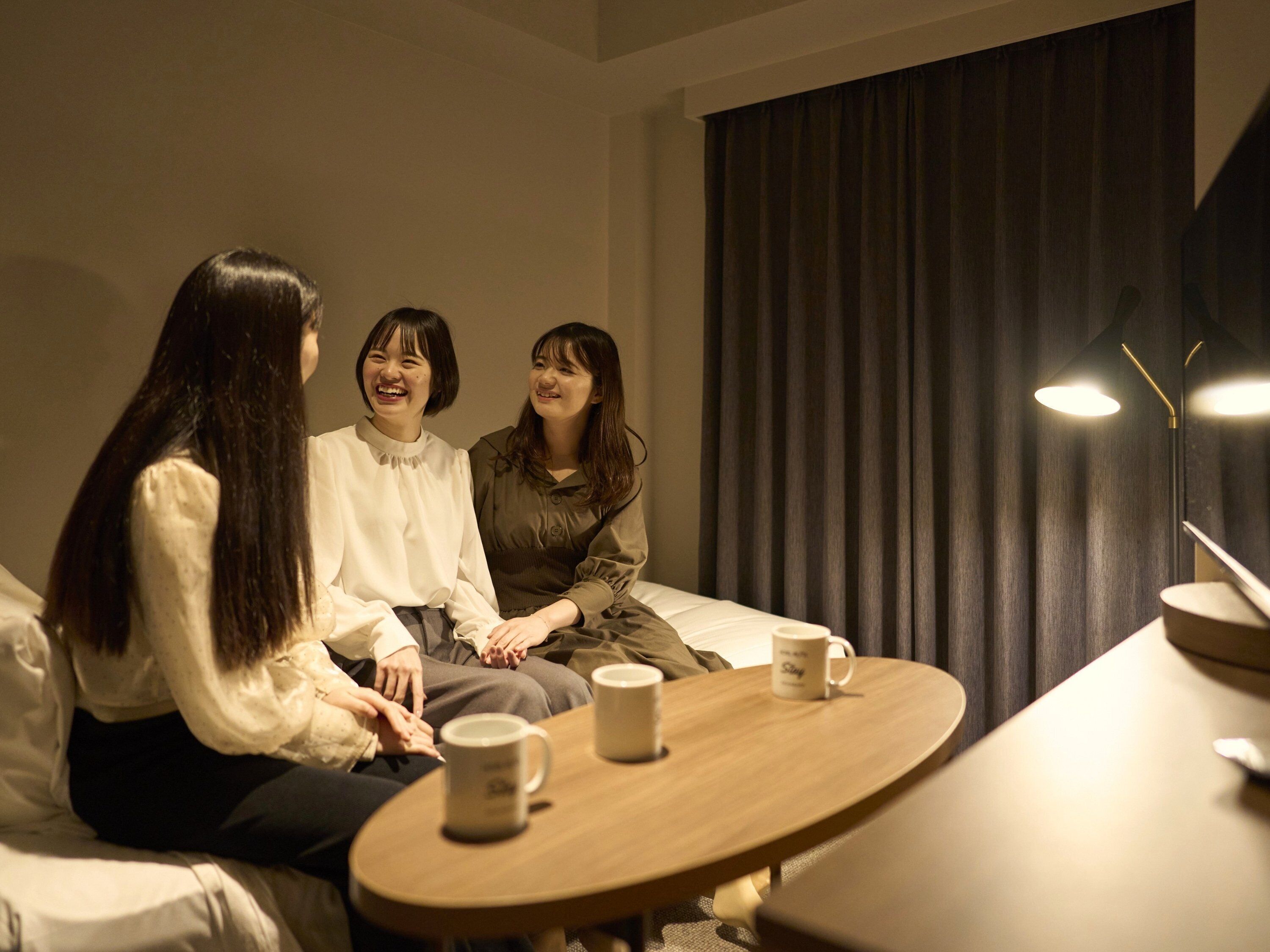 Une pièce comprenant un canapé, une table ronde avec deux tasses et une grande fenêtre avec des rideaux.