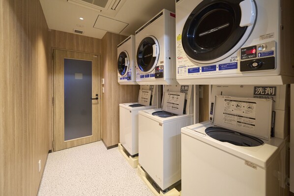 Une buanderie équipée de plusieurs machines à laver et de plusieurs sèche-linge, avec des murs en bois et un sol carrelé.