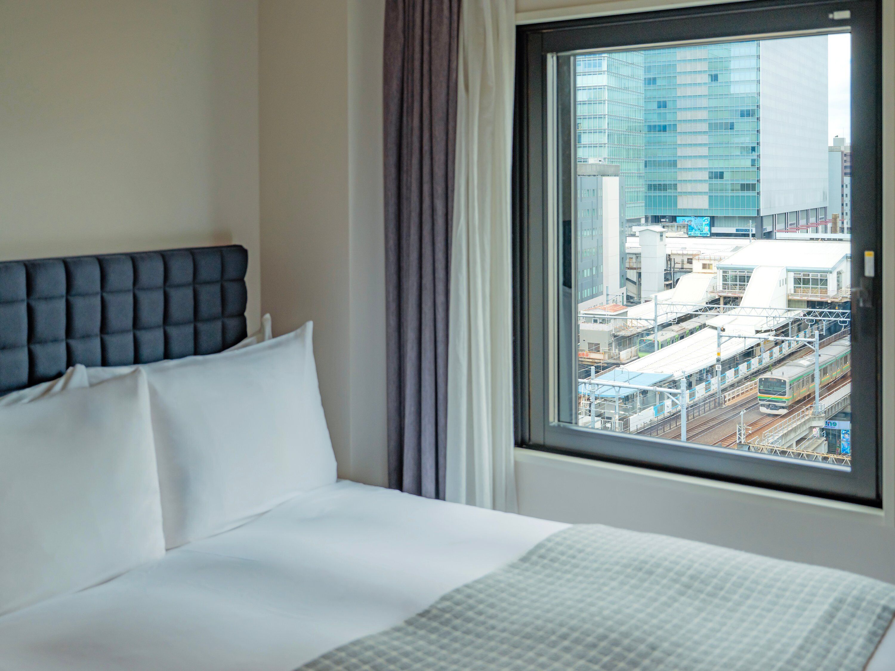 A hotel room with a bed, a window with a city view, and a curtain.