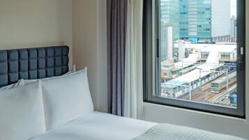 A hotel room with a bed, a window with a city view, and a curtain.