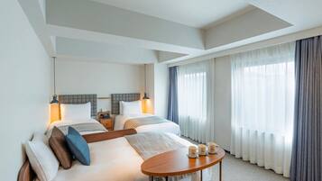 A hotel room with a large bed, bedside tables, a round table, and a view of the outdoors through sheer curtains.