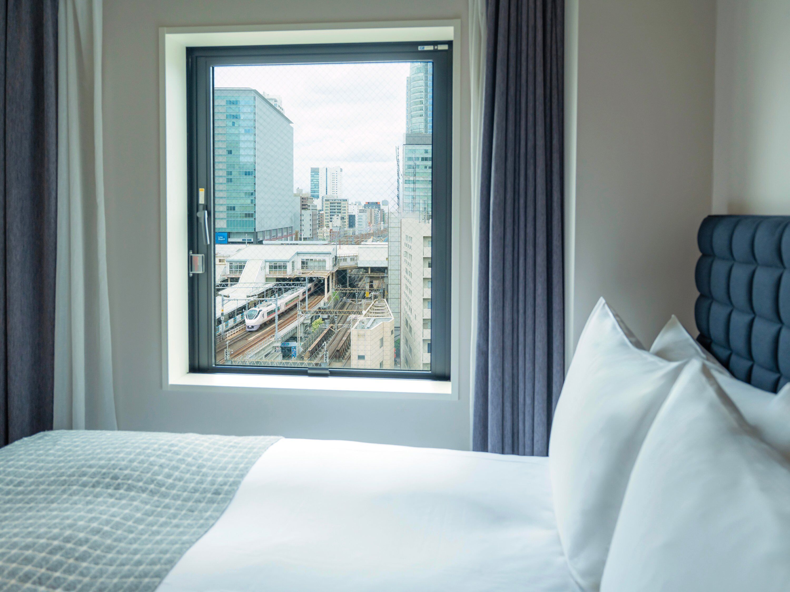 A hotel room with a large window offering a view of a cityscape and a train.