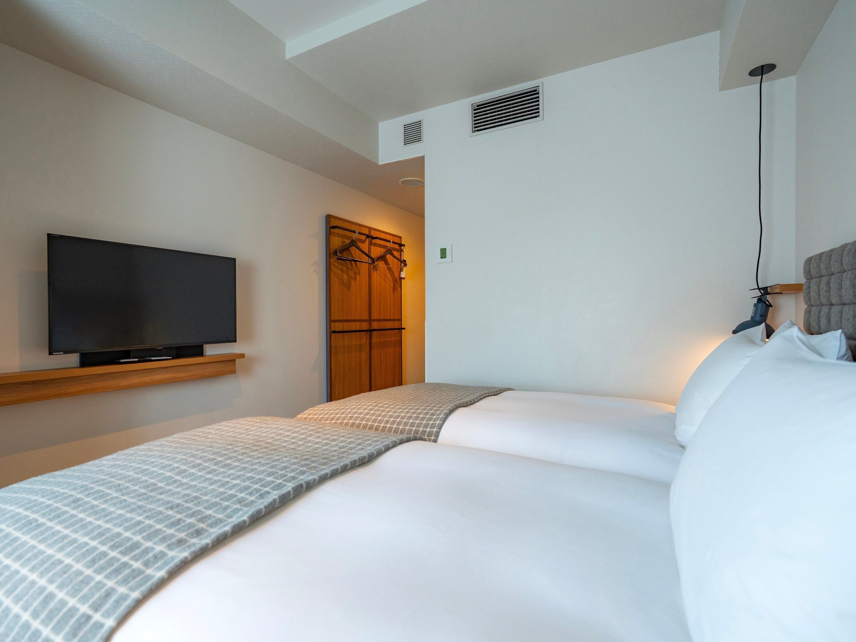 Habitación de hotel con televisor de pantalla plana montado en la pared, cama con colcha estampada y armario de madera con perchero.