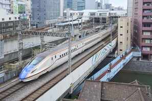 Un train à grande vitesse circulant sur une voie surélevée, avec une vue sur la ville en arrière-plan.