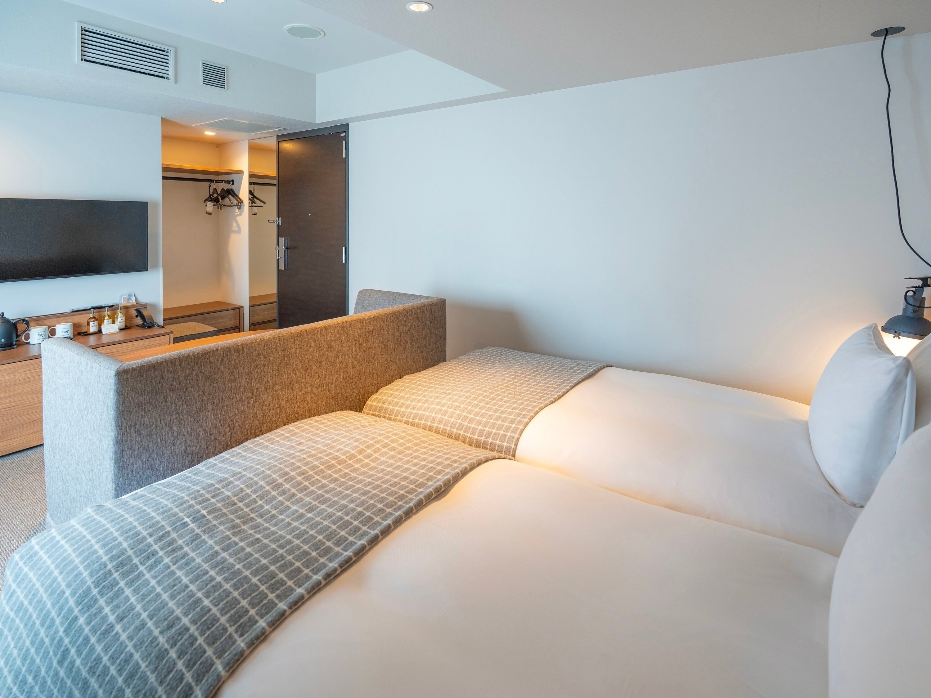 A modern hotel room with a sofa, a flat-screen TV, a desk with a lamp, and a wardrobe.