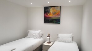 Une chambre avec deux lits simples, une table de chevet avec une lampe et un tableau au mur.