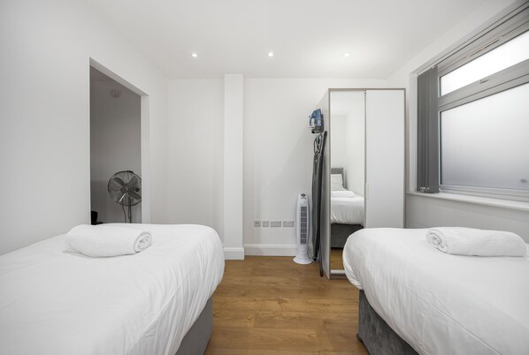 Ein Hotelzimmer mit zwei Einzelbetten, einem Heizlüfter, einem Spiegel und einem Fenster.