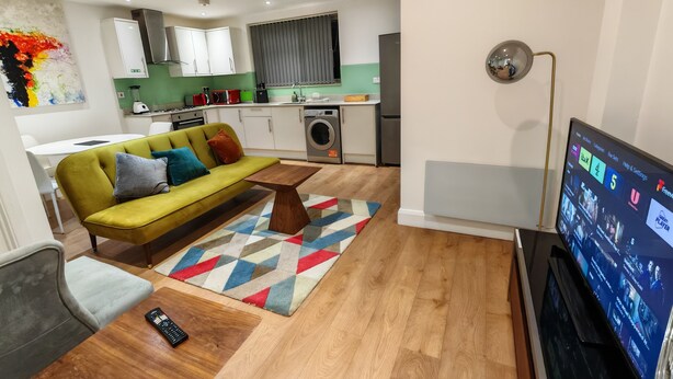 Un salon moderne avec un canapé, une table basse, un téléviseur et une cuisine en arrière-plan.