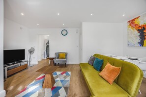 Ein modernes Wohnzimmer mit einem grünen Sofa, einem Flachbildfernseher und einem farbenfrohen Teppich.