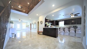 A spacious, well-lit kitchen with dark cabinets, a central island, and white chairs.