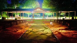 A covered outdoor area with benches and a central walkway, surrounded by trees.