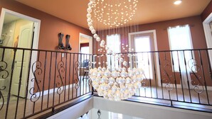 A spacious interior with a grand chandelier, a balcony with railings, and a seating area with chairs.